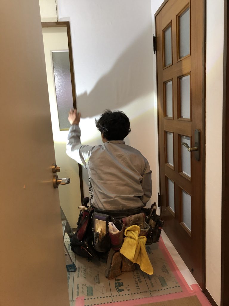 入間マンションリフォームで職人が壁のクロス張り替え作業をしている様子です。