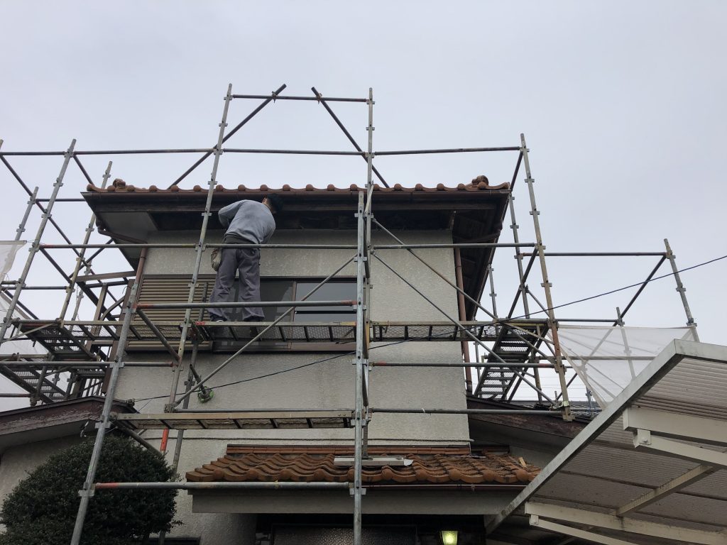 日高市中古住宅リフォームの塗装工事前の外観画像です。足場がかかり職人が作業している様子が写っています。