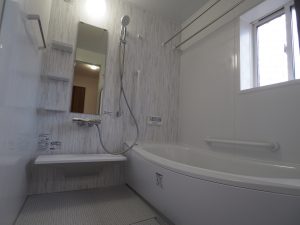 川越市新築戸建住宅システムバスルーム画像、グレーのアクセントパネルとシャワーバーと鏡が写っています。