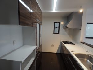 ふじみ野市内新築工事のキッチン、ホーロー素材のシステムキッチンは濃いブラウンの木目調です