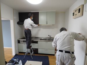 システムキッチン扉を木目調のブラウンカラーに張り替えています、職人2名が作業をしています。
