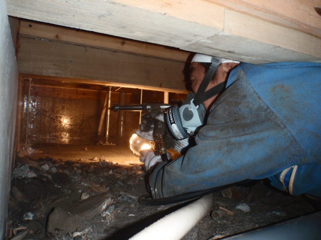 男性職人が床下に潜りシロアリの施工をしています。薬剤を散布しているところが写っています