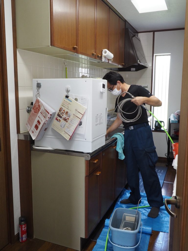 男性作業員がキッチンの排水口を高圧洗浄機のホースを入れて掃除をしているところが写っています