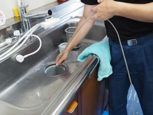 男性作業員がキッチンの排水管を高圧洗浄機で掃除をしています。