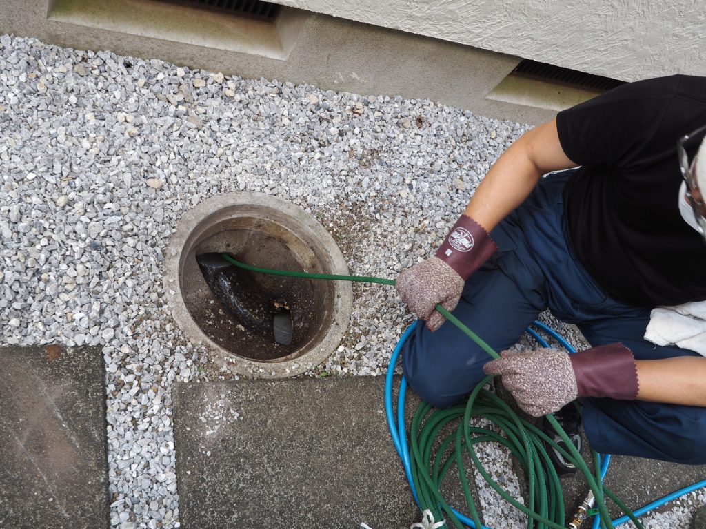 男性作業員が外部排水管を高圧洗浄機で掃除をしているところが写っています