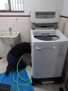 男性作業員が洗濯機付近排水を高圧洗浄機で掃除をしています