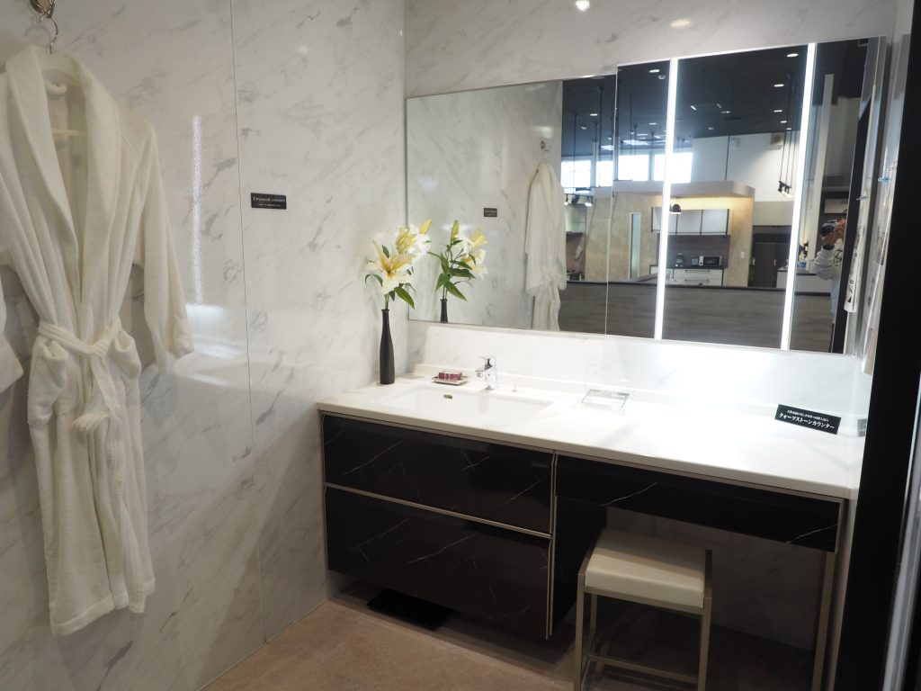 大宮のタカラスタンダードに展示されている洗面化粧台、黒い洗面パネルは高級感にあふれいてます。広い鏡と一凛の花、いす、バスローブが写っています。