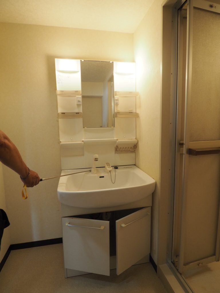 和光市マンションリフォームの施工前の洗面化粧台です。洗面化粧台の扉は少し開いています。人の腕が少し写っています。