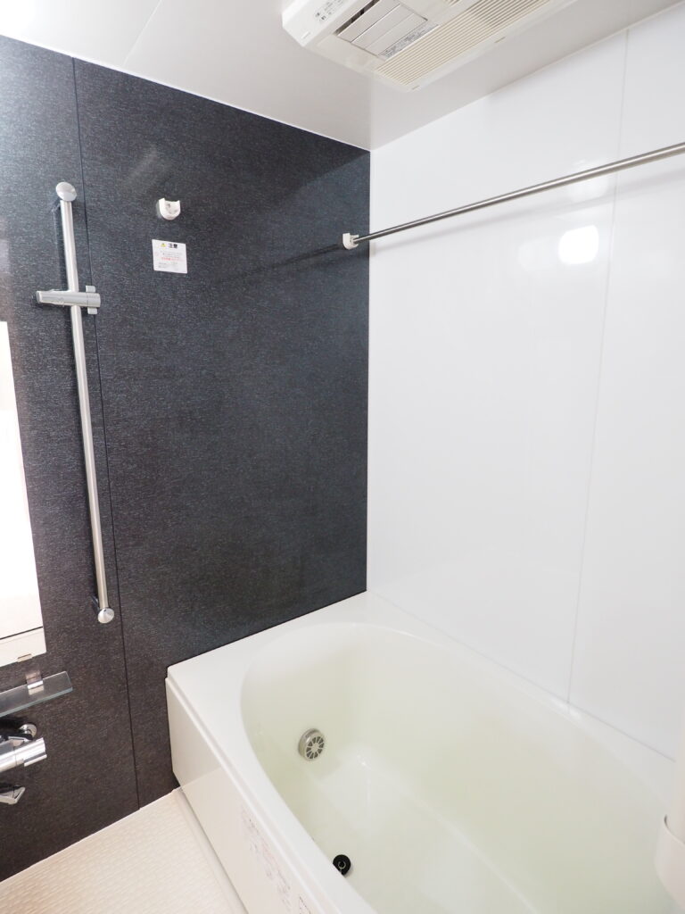 八王子中古マンション浴室、アクセントパネルがダーク系の色なのでシックな印象です。浴槽とシャワーバーに鏡などが写っています。