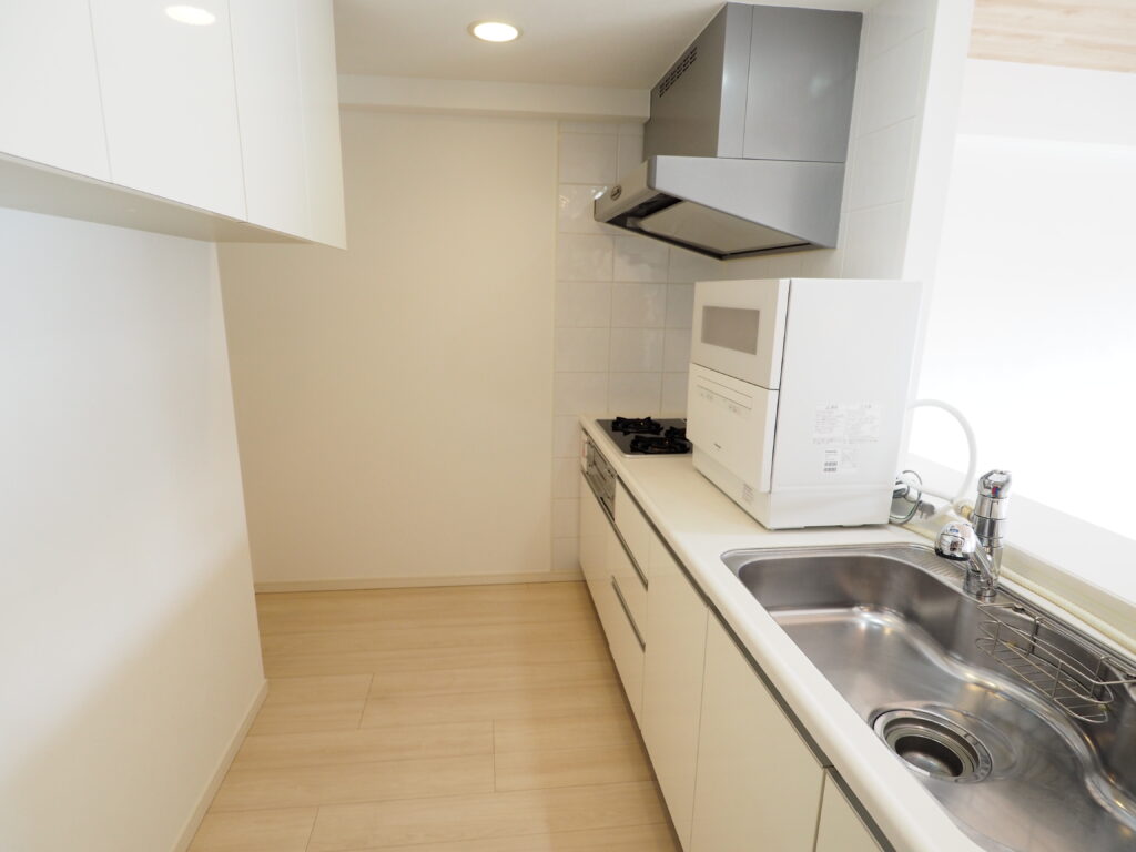 八王子市内マンションのリフォーム後のキッチン、白いシステムキッチンとシンクに換気扇、食洗器などが写っています。